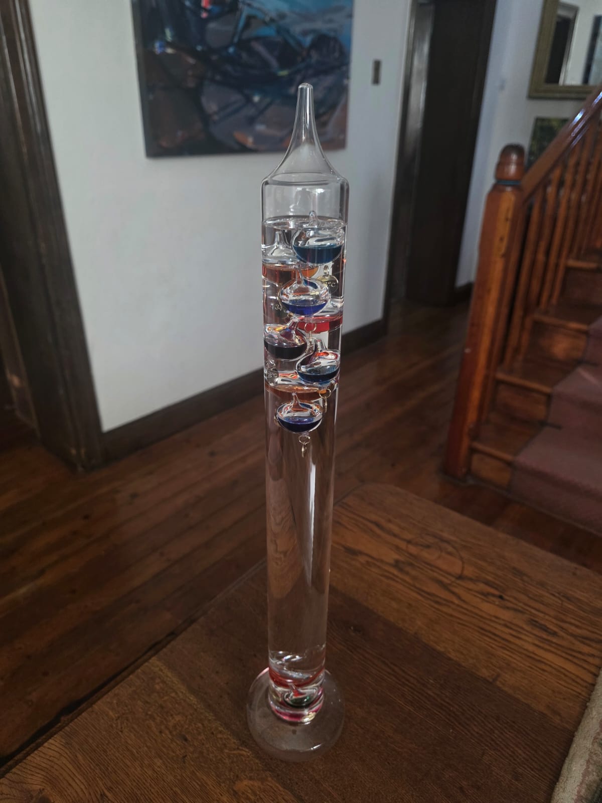 A Galileo thermometer photographed on a wooden floor in a hallway